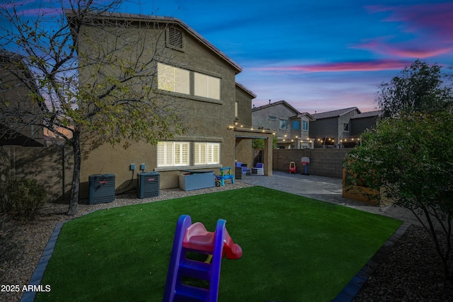 back house at dusk with a lawn, a patio, and central air condition unit