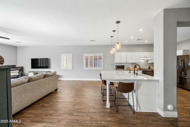 kitchen featuring a breakfast bar area, black fridge, white cabinetry, hanging light fixtures, and backsplash