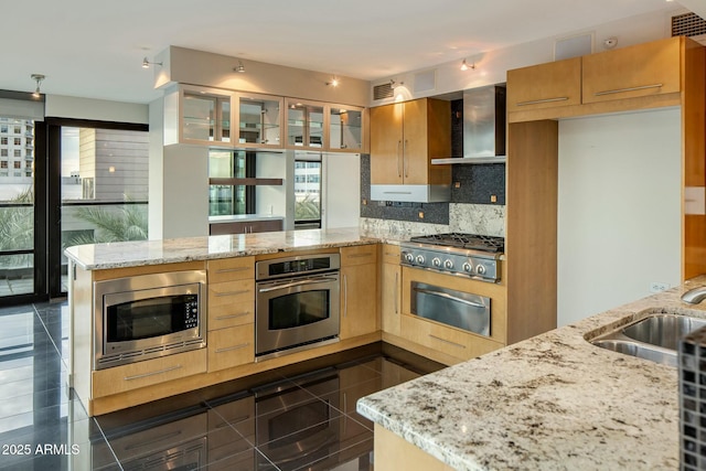 kitchen with kitchen peninsula, light stone counters, wall chimney exhaust hood, and stainless steel appliances