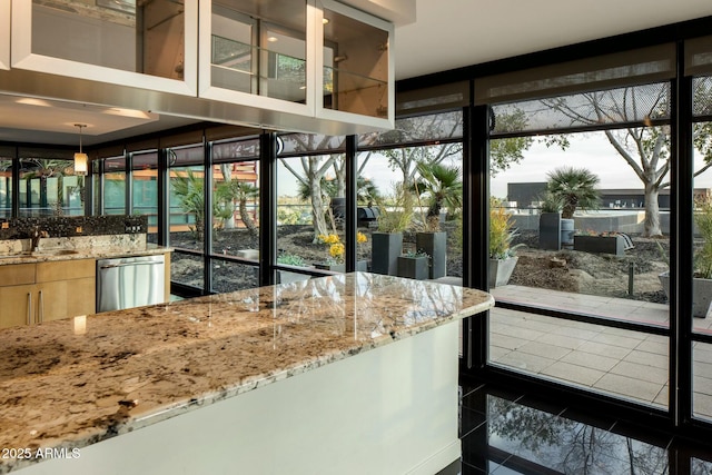 kitchen with light stone countertops, sink, pendant lighting, dark tile patterned flooring, and dishwasher