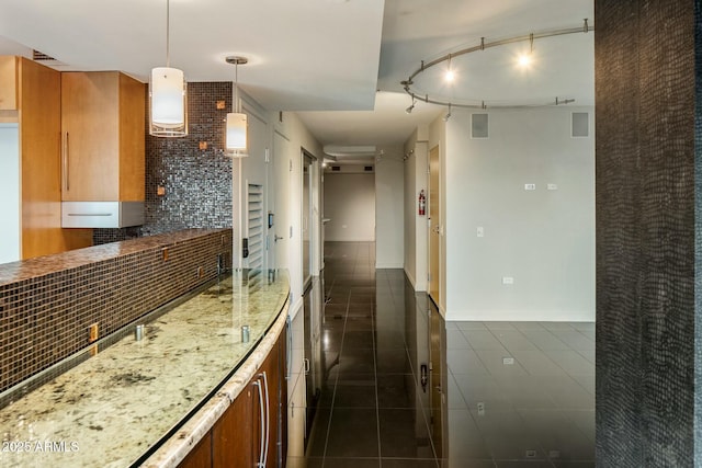 kitchen with track lighting, dark tile patterned flooring, decorative backsplash, decorative light fixtures, and light stone counters