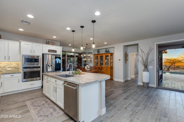 kitchen with light stone countertops, visible vents, a sink, decorative backsplash, and stainless steel appliances