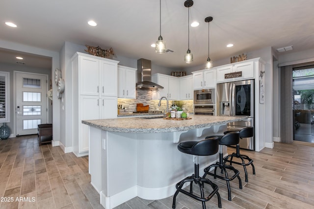 kitchen featuring backsplash, wall chimney range hood, white cabinets, stainless steel appliances, and a sink