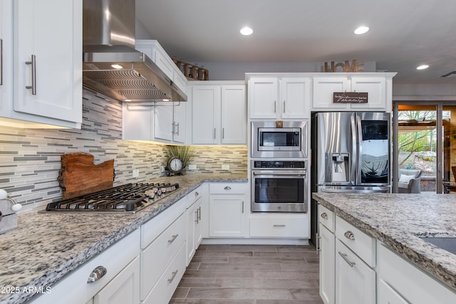 kitchen featuring backsplash, appliances with stainless steel finishes, white cabinets, and wall chimney range hood