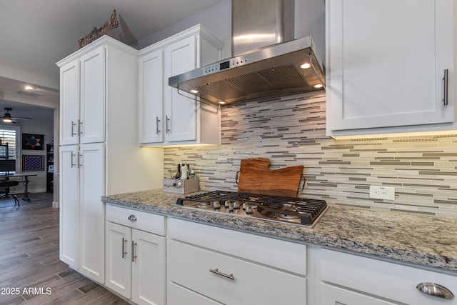 kitchen featuring ventilation hood, wood finished floors, stainless steel gas cooktop, white cabinets, and backsplash