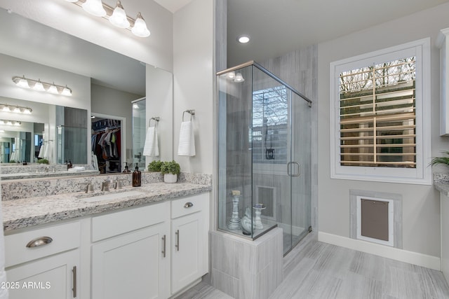 full bath with baseboards, vanity, a spacious closet, and a shower stall