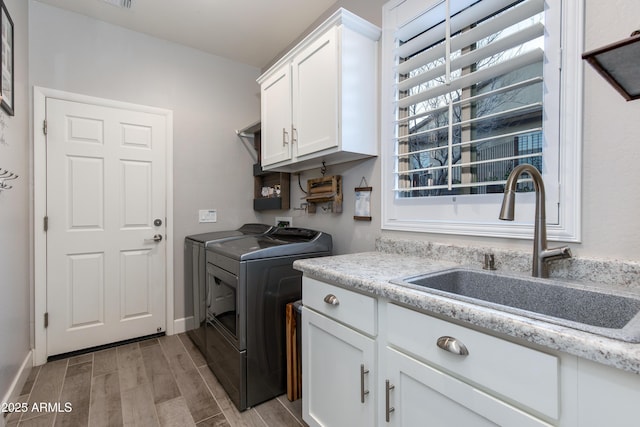 washroom featuring baseboards, wood finish floors, cabinet space, a sink, and washer and dryer