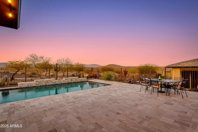 pool at dusk featuring outdoor dining space, a patio, and a fenced backyard