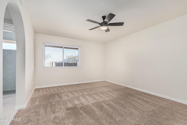 empty room featuring arched walkways, ceiling fan, baseboards, and carpet floors