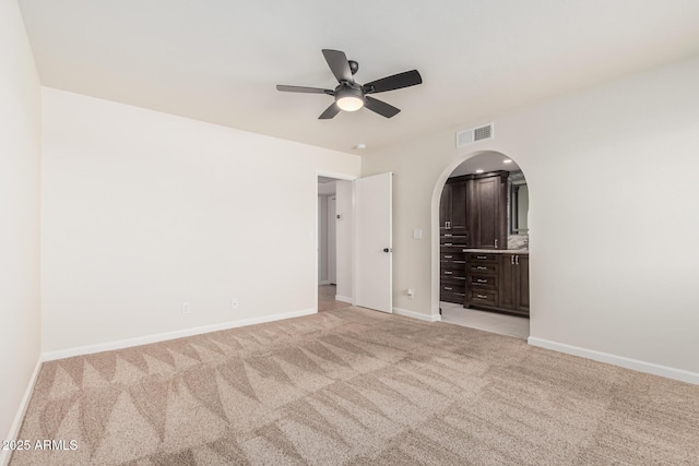 unfurnished bedroom featuring baseboards, visible vents, arched walkways, ceiling fan, and light carpet