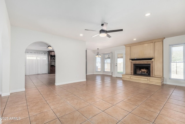 unfurnished living room featuring light tile patterned flooring, arched walkways, ceiling fan, and a fireplace