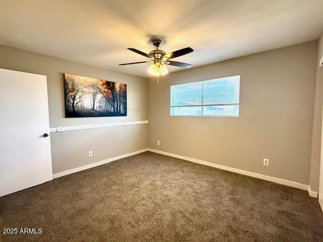 empty room featuring dark colored carpet, a ceiling fan, and baseboards