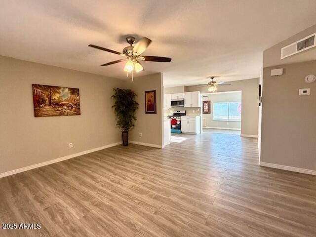 unfurnished living room featuring wood finished floors, visible vents, a ceiling fan, and baseboards