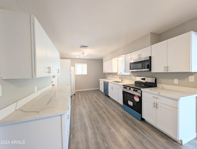 kitchen with light stone countertops, sink, appliances with stainless steel finishes, white cabinets, and light hardwood / wood-style flooring