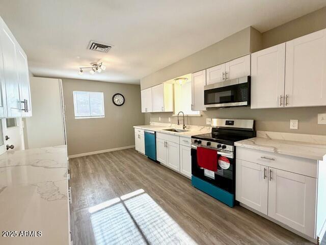 kitchen featuring stainless steel appliances, light wood finished floors, a sink, white cabinetry, and visible vents