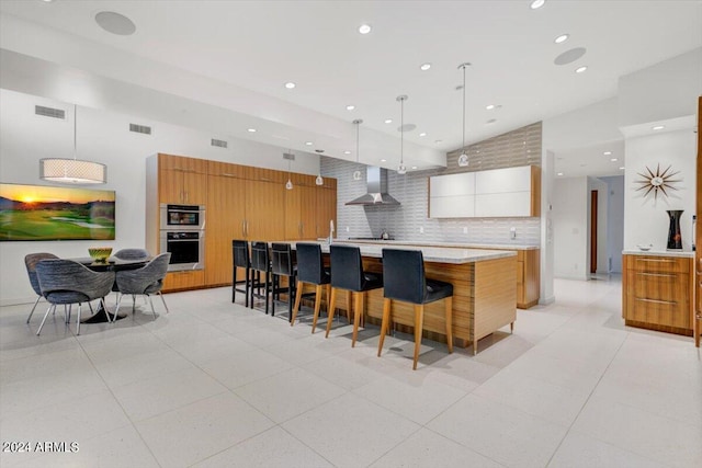 kitchen with a spacious island, white cabinets, wall chimney exhaust hood, tasteful backsplash, and light tile floors