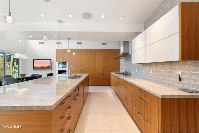 kitchen with decorative light fixtures, sink, white cabinetry, and wall chimney range hood