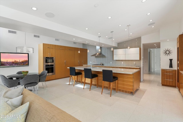 kitchen featuring hanging light fixtures, wall chimney range hood, a breakfast bar, backsplash, and a spacious island