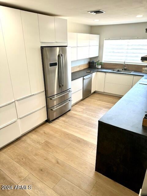 kitchen featuring white cabinets, stainless steel appliances, light wood-type flooring, and sink