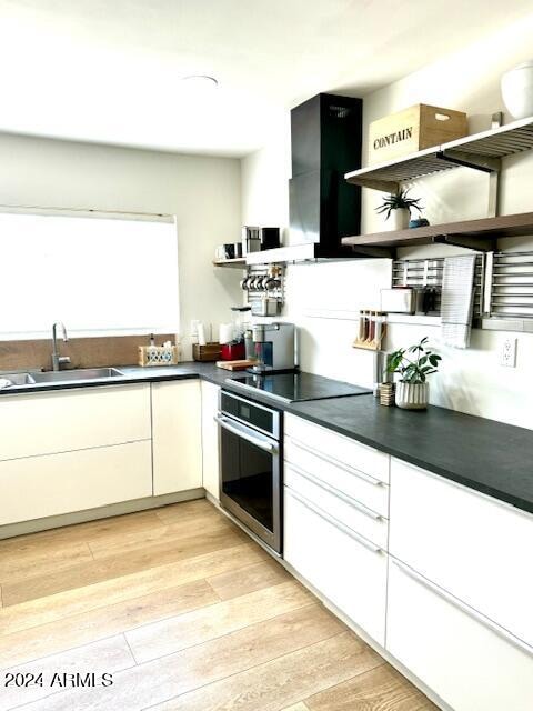 kitchen with sink, light hardwood / wood-style flooring, white cabinetry, black electric cooktop, and stainless steel oven