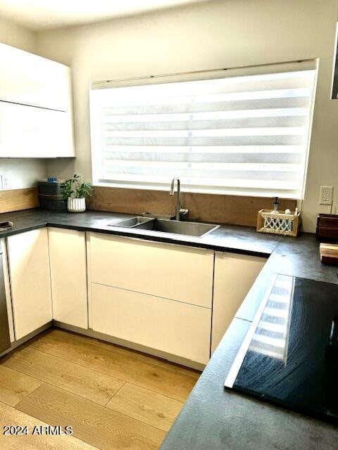 kitchen featuring light wood-type flooring, sink, cooktop, and white cabinetry