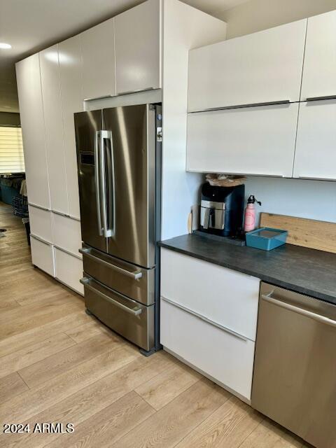 kitchen with stainless steel appliances, white cabinetry, and light wood-type flooring