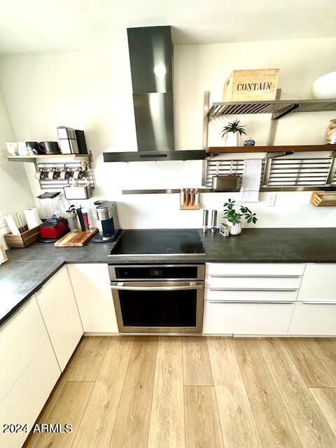 kitchen with white cabinets, light hardwood / wood-style flooring, ventilation hood, stainless steel oven, and black electric stovetop