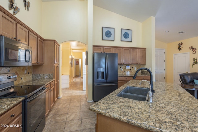 kitchen with tasteful backsplash, black appliances, stone counters, a kitchen island with sink, and sink