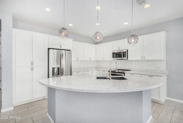 kitchen featuring appliances with stainless steel finishes, a kitchen island with sink, pendant lighting, and white cabinetry