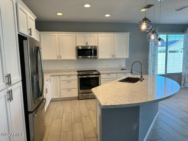 kitchen featuring sink, white cabinetry, a center island with sink, appliances with stainless steel finishes, and decorative light fixtures