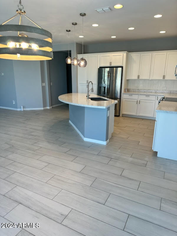 kitchen featuring pendant lighting, white cabinets, sink, a center island with sink, and stainless steel fridge with ice dispenser