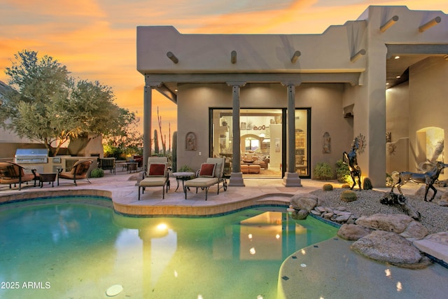 pool at dusk with area for grilling and a patio