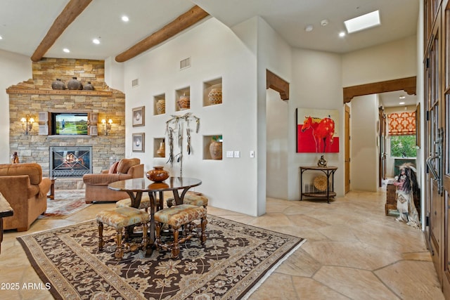 dining area featuring a high ceiling, a skylight, a stone fireplace, and beamed ceiling