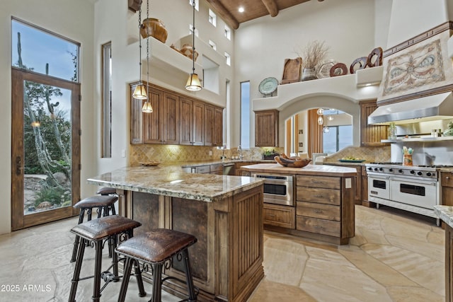 kitchen featuring appliances with stainless steel finishes, a breakfast bar, pendant lighting, light stone counters, and wall chimney exhaust hood