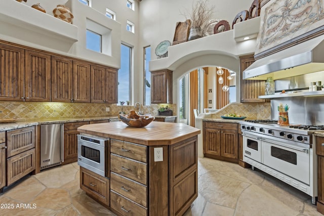 kitchen with a kitchen island, appliances with stainless steel finishes, ventilation hood, wooden counters, and backsplash