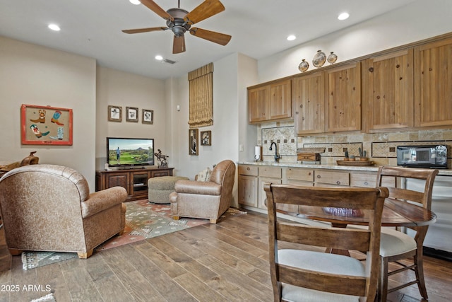 kitchen with sink, backsplash, hardwood / wood-style flooring, ceiling fan, and light stone countertops