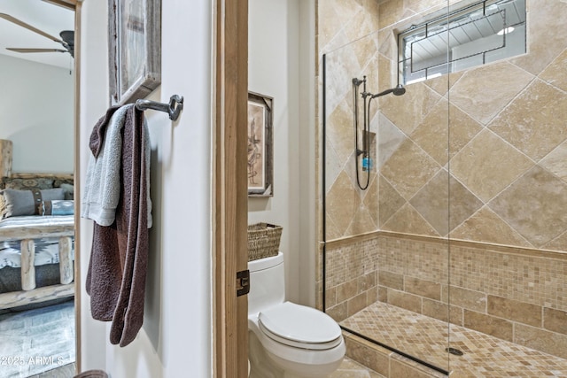 bathroom featuring ceiling fan, a shower with door, and toilet