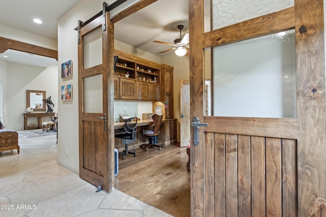 home office with a barn door, built in desk, ceiling fan, and light hardwood / wood-style flooring