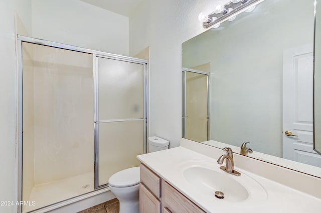 bathroom featuring toilet, vanity, tile patterned flooring, and a shower with door