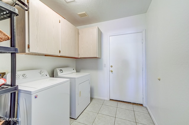 laundry room featuring light tile patterned floors, washing machine and dryer, a textured ceiling, and cabinets