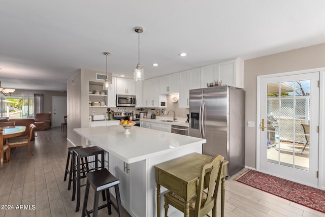 kitchen featuring appliances with stainless steel finishes, hanging light fixtures, light countertops, white cabinetry, and a sink