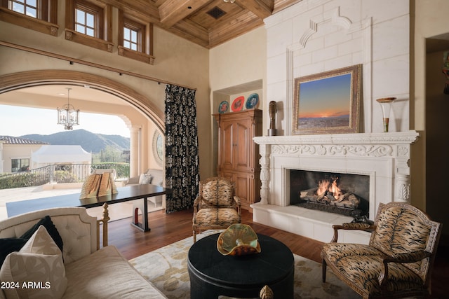 living room featuring coffered ceiling, a tiled fireplace, beamed ceiling, hardwood / wood-style floors, and a high ceiling