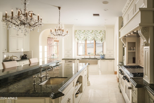 kitchen with a notable chandelier, hanging light fixtures, sink, cream cabinetry, and dark stone counters