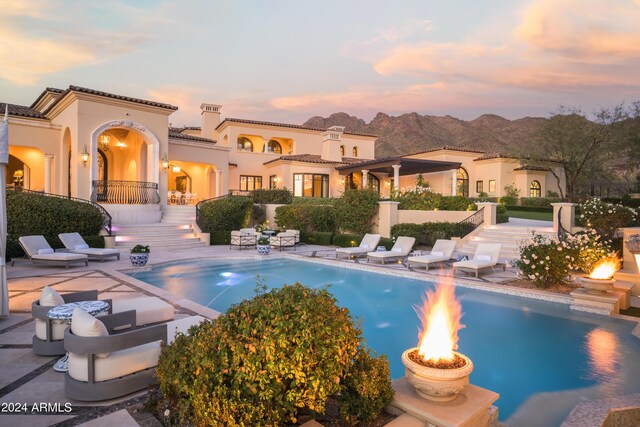 pool at dusk featuring a patio, an outdoor fire pit, and a mountain view