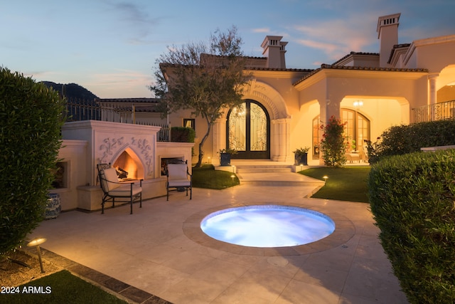 pool at dusk with an outdoor fireplace and a patio area