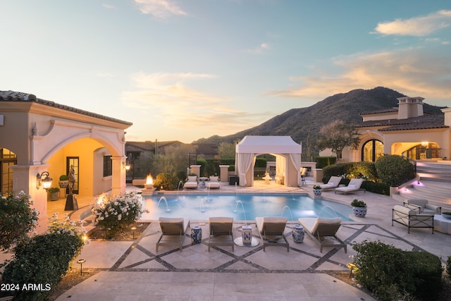 pool at dusk featuring pool water feature, a mountain view, and a patio area