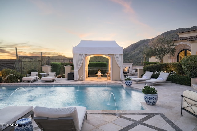 pool at dusk featuring pool water feature, an outdoor hangout area, a mountain view, and a patio