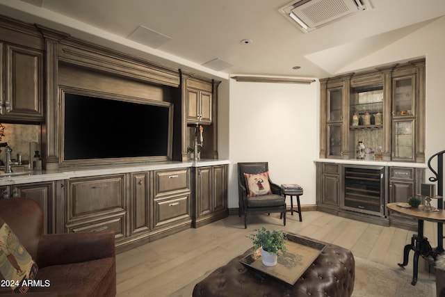 living room with beverage cooler, light hardwood / wood-style floors, indoor bar, and vaulted ceiling