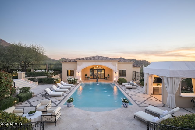 pool at dusk featuring outdoor lounge area, a patio area, a mountain view, and french doors