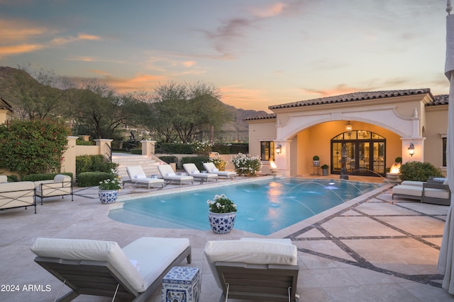 pool at dusk featuring french doors, an outdoor living space, a patio, and pool water feature